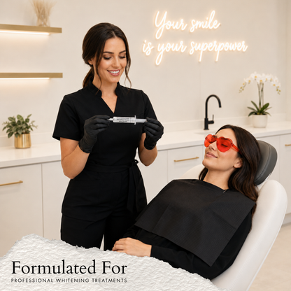 A professional teeth whitening provider in black scrubs holds a White in Minutes® 16% hydrogen peroxide whitening gel syringe beside a reclined client wearing red protective glasses in a modern treatment studio.