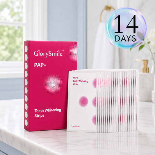 Teeth whitening strips kit displayed on a marble bathroom counter with a pink PAP+ box and 14 individually wrapped strips neatly arranged in overlapping rows, styled in a clean, modern setting with soft natural light.