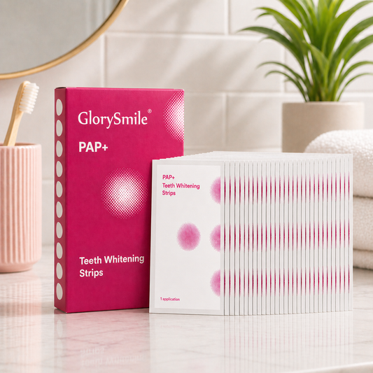 Teeth whitening strips kit displayed on a marble bathroom counter with a pink PAP+ box and 14 individually wrapped strips neatly arranged in overlapping rows, styled in a clean, modern setting with soft natural light.