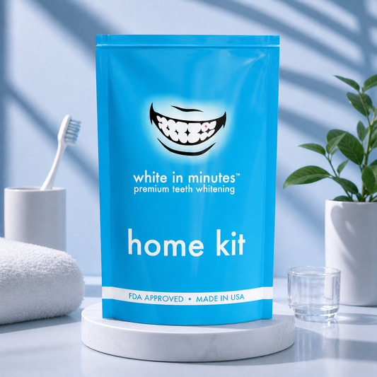 White in Minutes home teeth whitening kit pouch displayed on a white marble pedestal in a clean bathroom setting with soft blue lighting and minimal accessories, showcasing at-home whitening product made in the USA.